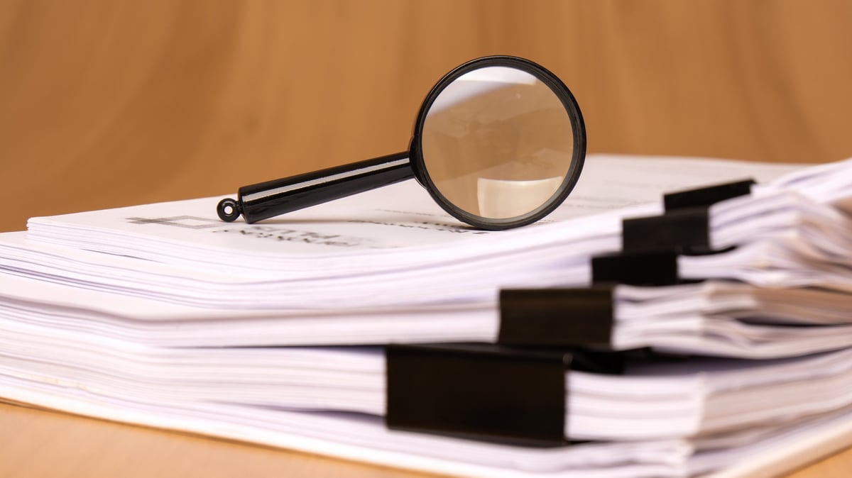 A magnifying glass rests on scattered clipped papers, symbolizing diligent research and careful analysis