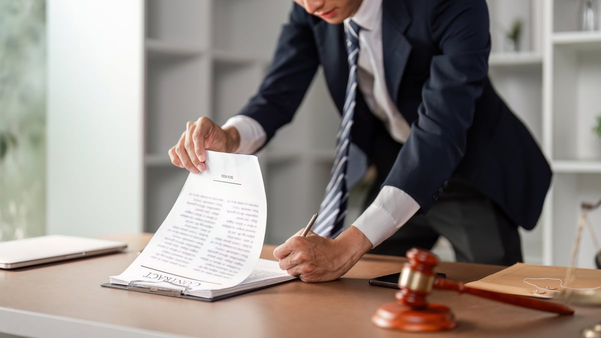 A young Asian lawyer is reviewing and signing legal contract documents at his office desk, dedicated to his law practice.