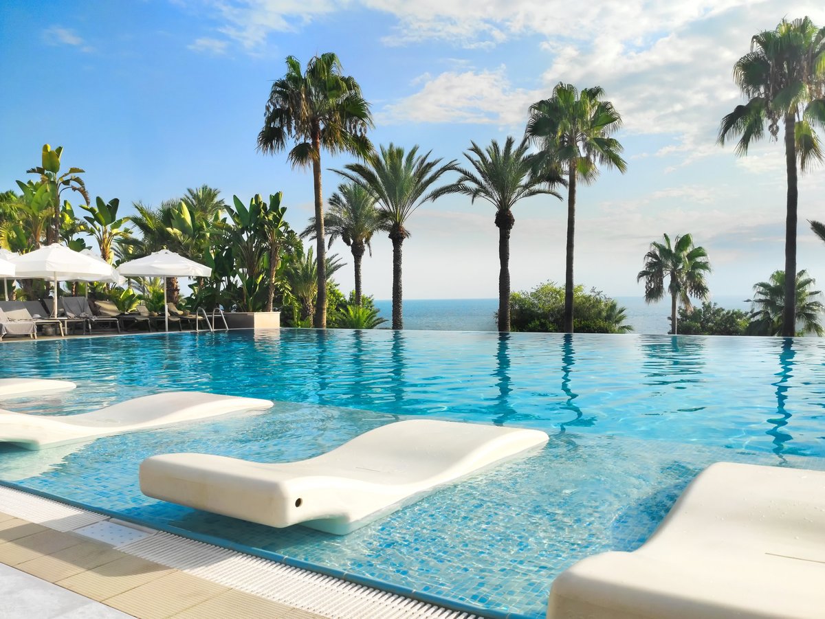 Stunning resort pool, surrounded by loungers, palms, and ocean views, is perfect for a getaway